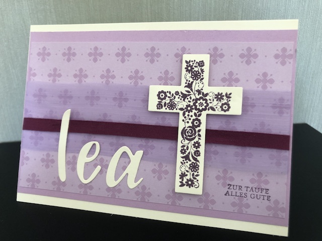 Zusehen ist eine selbst gebastelte Karte zur Taufe. Die Karte ist in lila Tönen gehalten, der Name Lea ist ausgestanzt auf die Karte geklebt, neben dem Namen ist ein florales Kreuz angebracht.