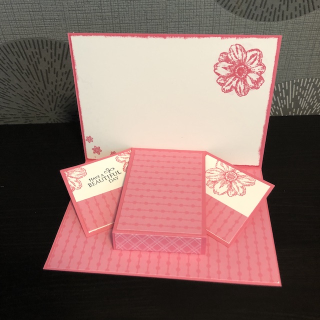 Zu sehen ist der Innenteil einer Pop Up Karte mit Flügeln. Die Seite die hochkant steht ist hell mit einer einzelnen rosa Blüte, der untere Teil ist rosa. Die zwei Flügel die heraus poppen sind zur Hälfte rosa und zu anderen Hälfte mit Blümchen bestempelt auf dem linken Flügel steht: Have a Beautiful Day.