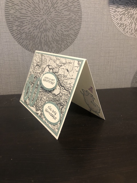 Zu sehen ist eine Geburtstagskarte mit einer 60 drauf. Der Hintergrund ist eine Landkarte in schwarz weiß. Zwei Texte sind auf der Karte angebracht: Hurra du hast Geburtstag, Fühl dich geknuddelt. Im Innenteil ist ein tanzendes Schaf mit Partyhut zu sehen.