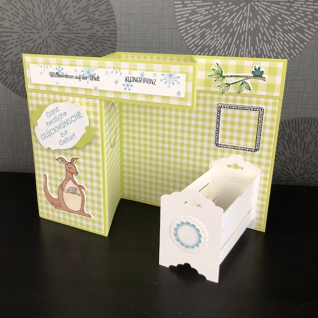 Double Z Fold Babycards. Eine Babykarte mit Effekt. Zu sehen ist eine Karte mit einem weißen Kinderbettchen. An der vermeintlichen Wand hängen leere Bilderrahmen, in die die Daten des Babys eingetragen werden können.