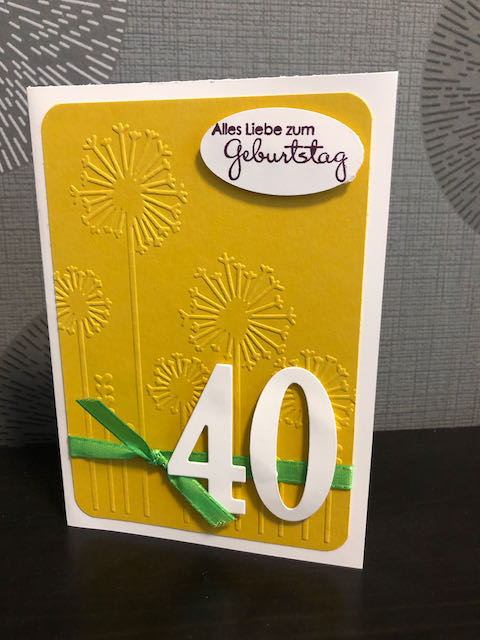 Geburtstagskarte in Honiggelb mit geprägten Pusteblumen, grünem Band und der Zahl 40 oben drauf. Der Spruch auf der Karte lautet: Alles Liebe zum Geburtstag. 