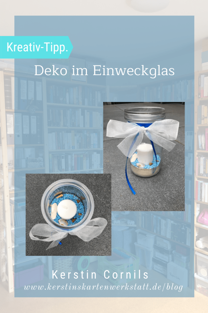 Ein 1,5l Einmachglas gefüllt mit Vogelsand. Darüber sind blaue Steinchen gestreut auf denen Muscheln und Schnecken aus dem Meer liegen. In der Mitte steckt eine weiße Stumpen Kerze. Das Weckglas ist oben mit einer weißen Taftschleife versehen und blauen Bändern.