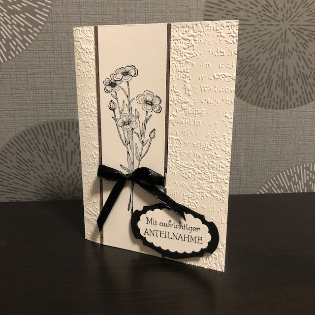 weiße Trauerkarte mit Prägung und gestempelten Blumen in Grau mit schwarzer Schleife und Spruch: Mit aufrichtiger Anteilnahme.