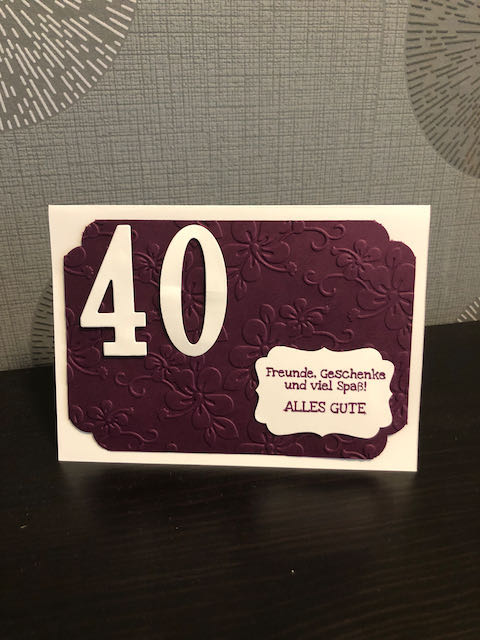 Selbst gebastelte Karte zum 40. Geburtstag. Die Grundkarte ist weiß. Darauf wurde ein mit Blumen geprägter Cardstock in Brombeermousse geklebt. Die Ziffern 4 und 0 nehmen etwa ein viertel der Karte ein. Auf einem Etikett steht der Spruch: Freunde, Geschenke und viel Spaß! Alles Gute