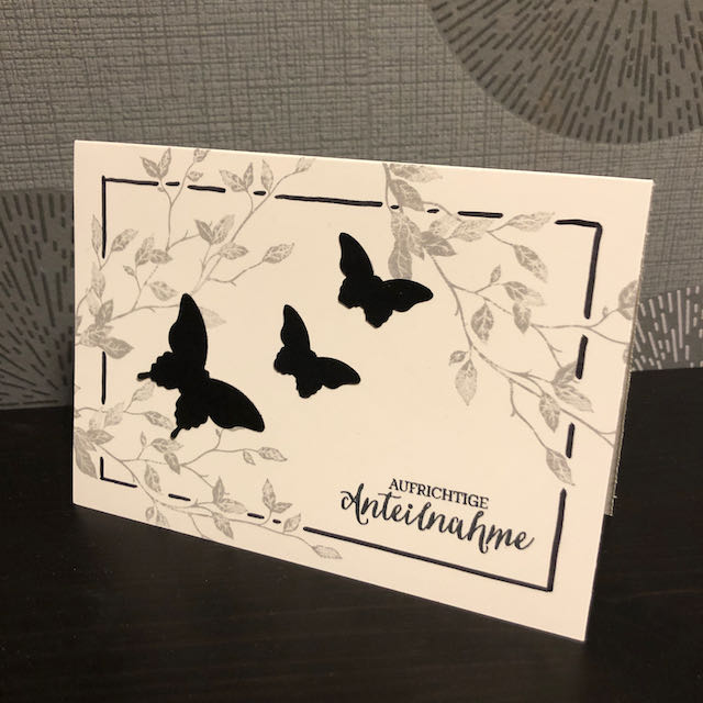 Trauerkarte mit Blätterranken und schwarzen Schmetterlingen, die symbolisch gen Himmel fliegen.