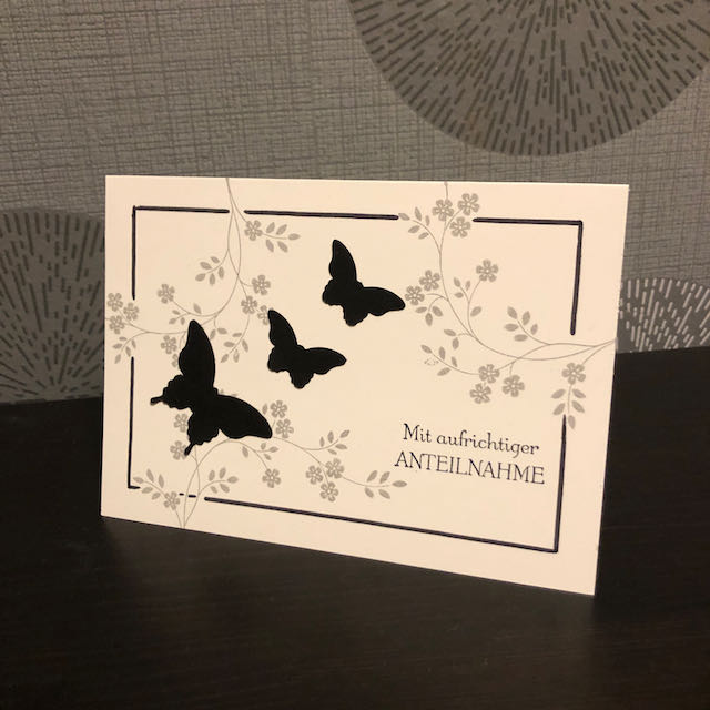 Trauerkarte mit Blätterranken und schwarzen Schmetterlingen, die symbolisch gen Himmel fliegen.