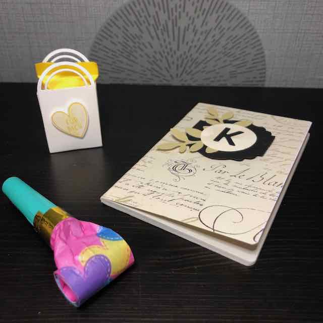 Foto von den Goodies im Materialpaket: eine Tröte, ein Notizbuch mit meinem Anfangsbuchstaben und eine Minitasche mit Schokolade drin