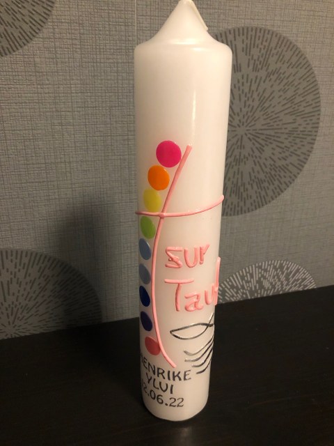 Kerze zur Taufe selbstgemacht mit Kreisen in Regenbogenfarben, einem Kreuz in Rosa und der Beschriftung in Silber