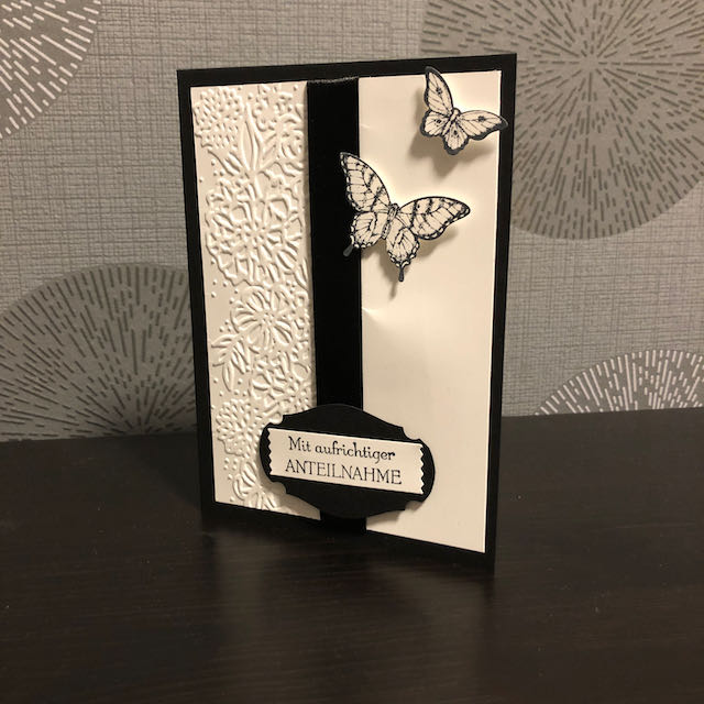 gebastelte Trauerkarte in schwarz weiß mit geprägten Blumen, einem schwarzen Band in der Mitte und zwei Schmetterlinge am oberen Rand. Der Spruch auf der Karte lautet: Mit aufrichtiger Anteilnahme