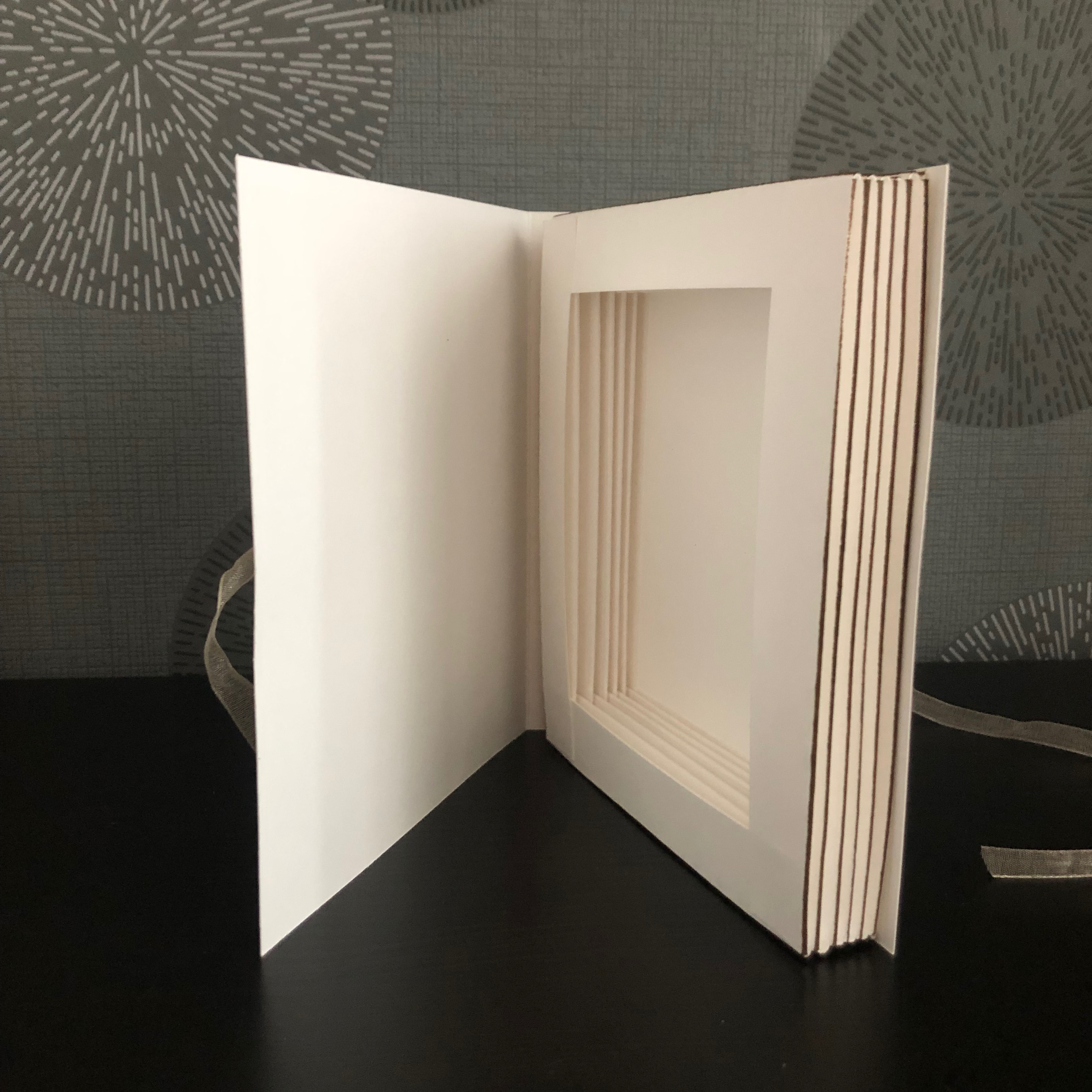 Eine kleine gebastelte Box im Buchformat. Vorne drauf sind zwei Weinflaschen aufgeklebt und der Spruch: Botschaft mit Lieben Grüßen. Die Box wird mit einem Band verschlossen.