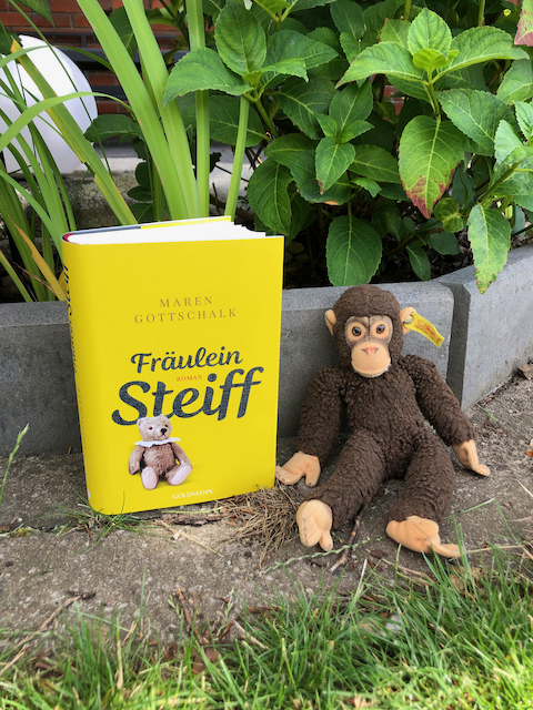 Der biografische Roman über Magerete Steiff mit einem Steiff Affen vor einem Blumen Beet: Fräulein Steiff von Maren Gottschalk