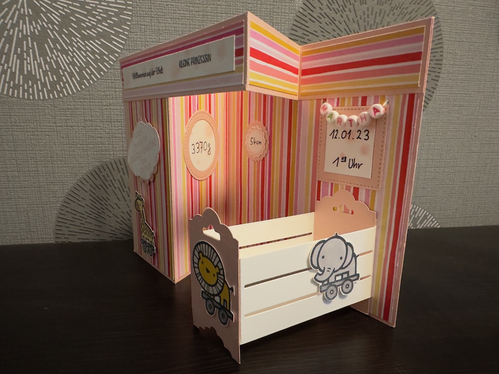 Z Fold Babykarte in rosa für ein Mädchen. Die Karte steht von alleine durch das Babybett, dass sich ausklappen lässt. Der Name hängt in einer Perlenkette über dem Bett.