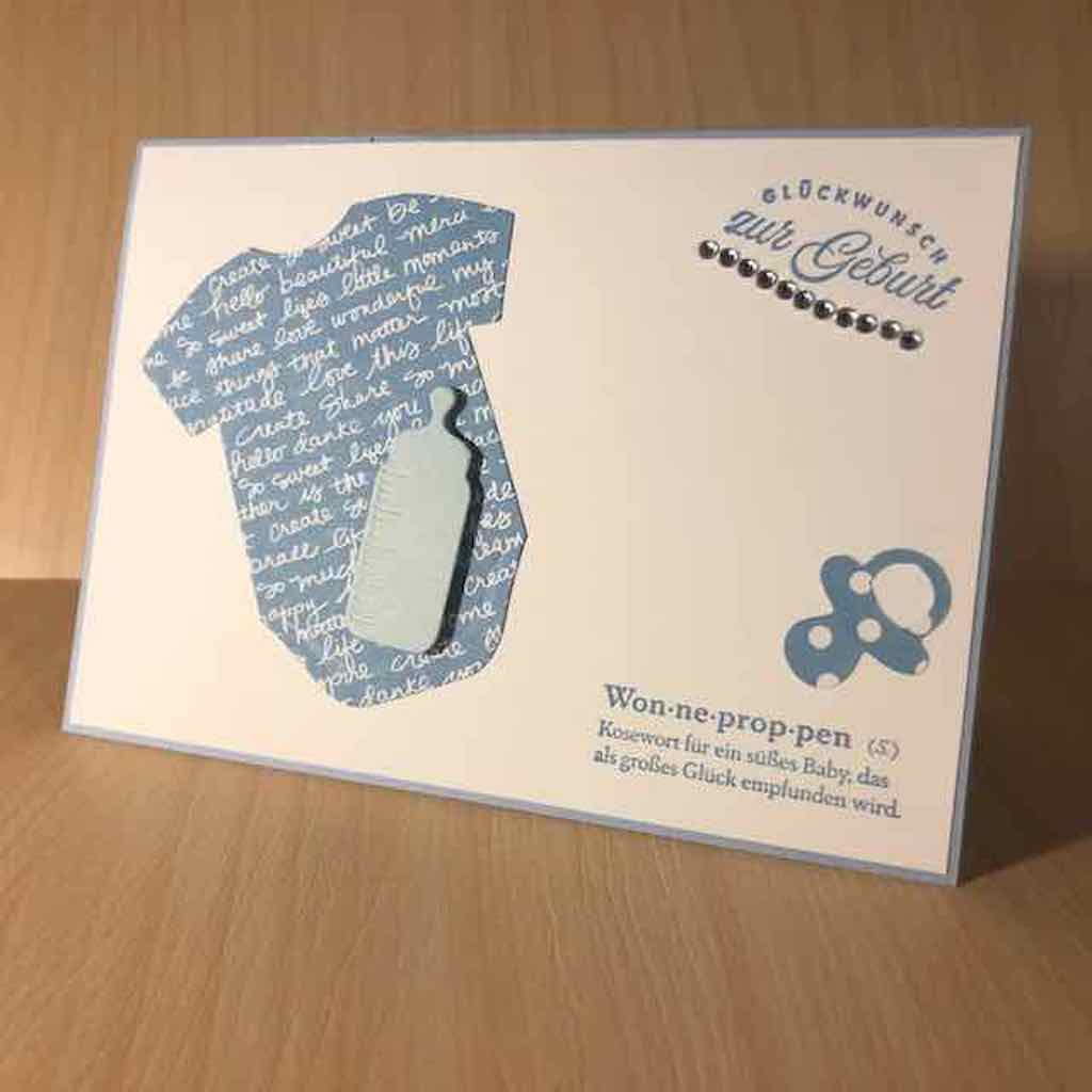 Babykarte selbstgemacht in verschiedenen Blautönen kombiniert mit weiß. Als Applikationen sind zu sehen ein Schnuller, eine Trinkflasche und ein Babybody