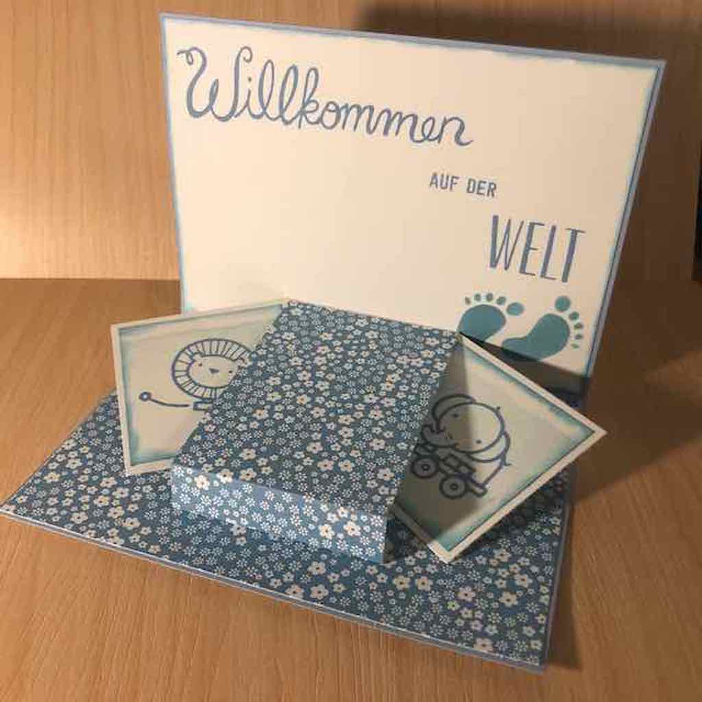 Babykarte selbstgemacht in verschiedenen Blautönen kombiniert mit weiß. Die Karte hat im Inneren ein Pop-up-Element. Es kommen ein kleiner Löwe und ein kleiner Elefant zum Vorschein.