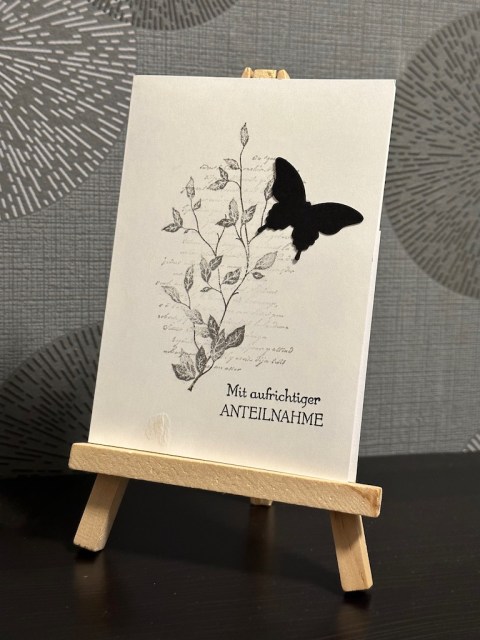 Trauerkarte mit Ranke, verschwommener Schrift und einem schwarzen Schmetterling