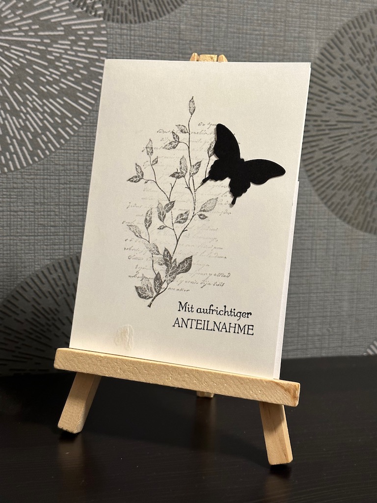 Trauerkarte mit Ranke, verschwommener Schrift und einem schwarzen Schmetterling