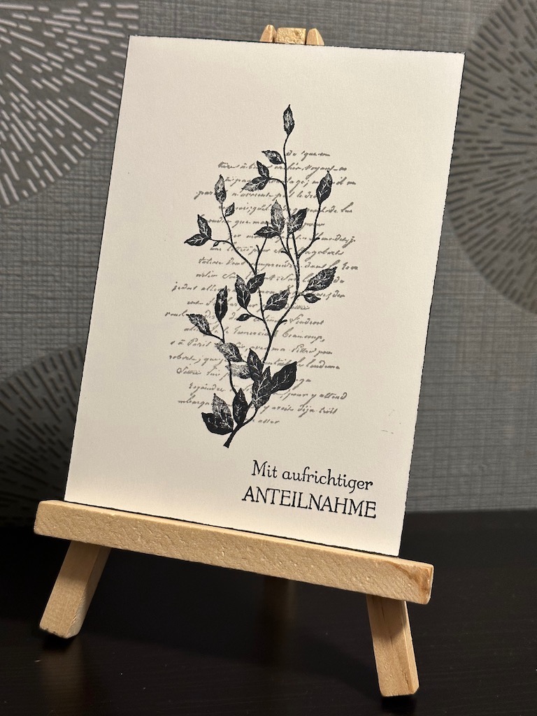 Trauerkarte in schwarz weiß mit Schriftstempel und darüber einen Zweig mit Blättern. Als Spruch ist: Mit aufrichtiger Anteilnahme auf die Karte gestempelt.
