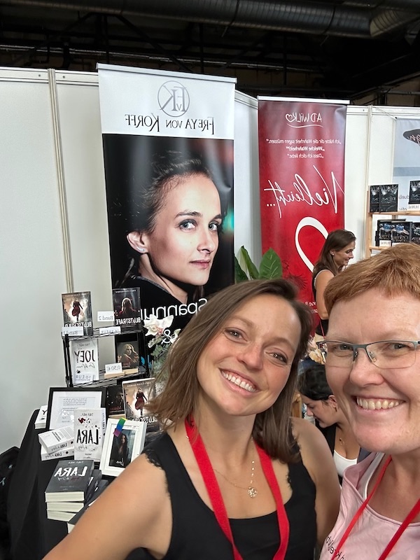 Ein Foto mit der Autorin A.D. Wilk und Kerstin alias Kerstins Kartenwerkstatt. Im Hintergrund ist Freya von Korff zu sehen. Das Foto entstand auf der Buch Berlin 2023
