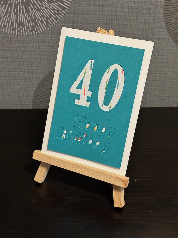 Geburtstagskarte in Bermudablau zum 40. Geburtstag. Die 40 ist in großen Ziffern ausgestanzt und mit einem Designpapier hell hinterlegt. Ganz unscheinbar erkennt man ein gestanztes Happy Birthday unter der Zahl.