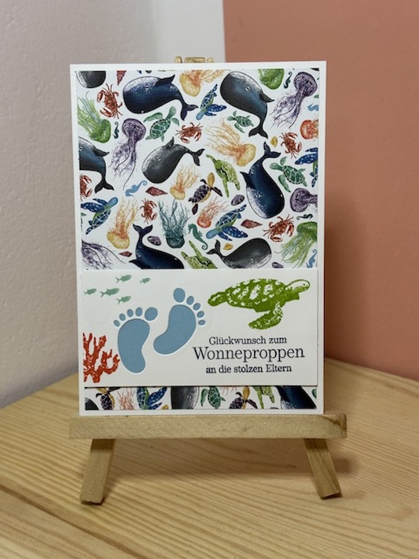 Zu sehen ist eine Glückwunschkarte zur Geburt. Auf der Babykarte ist der Spruch: "Glückwunsch zum Wonneproppen an die stolzen Eltern" gestempelt. Der Hintergrund ist durch das Designpapier mit Meerestieren einfach bunt und kann sowohl für Mädchen, als auch für Jungen verschenkt werden.