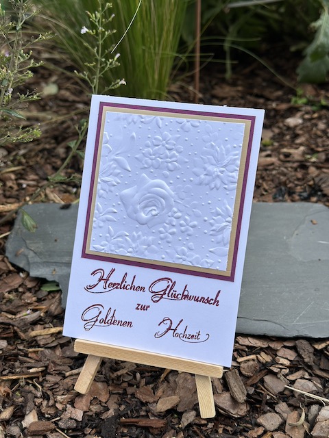 Zu sehen ist eine Karte zur goldenen Hochzeit. In weiß geprägt mit dem Prägefolder Feldblumen kann man eine Rose erkennen. Dahinter verbirgt sich eine goldene Mattung. Darunter steht: Herzlichen Glückwunsch zur goldenen Hochzeit. Gebastelt mit Material von Stampin Up