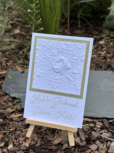 Zu sehen ist eine Karte zur goldenen Hochzeit. In weiß geprägt mit dem Prägefolder Feldblumen kann man eine Rose erkennen. Dahinter verbirgt sich eine goldene Mattung. Darunter steht: Herzlichen Glückwunsch zur goldenen Hochzeit. Gebastelt mit Material von Stampin Up