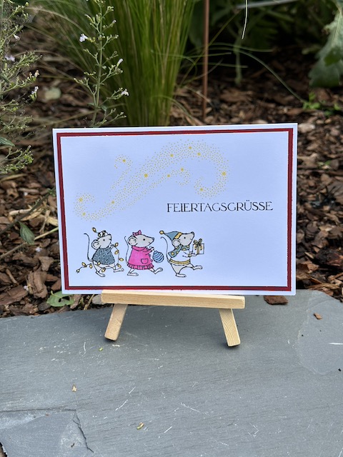 Zu sehen ist eine Weihnachtskarte mit den Festagsmäusen. Die drei Mäuse, die mit dem Stempelset: Festagsmäuse gestempelt wurden sind bunt angemalt. Als Spruch steht auf der Karte: Festagsgrüße. Über den Mäusen kann man ganz schwach in gelb sinnbildlich die Milchstraße sehen.
