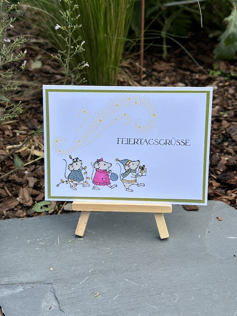 Zu sehen ist eine Weihnachtskarte mit den Festagsmäusen. Die drei Mäuse, die mit dem Stempelset: Festagsmäuse gestempelt wurden sind bunt angemalt. Als Spruch steht auf der Karte: Festagsgrüße. Über den Mäusen kann man ganz schwach in gelb sinnbildlich die Milchstraße sehen.