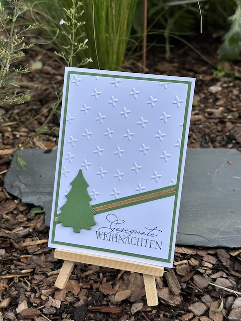 ZU sehen ist eine Weihnachtskarte ganz schlicht in weiß und grün. Der obere Teil ist mit Sternchen Muster geprägt. Auf der diagonalen Grenze zum glatten Teil ist ein Streifen gold zusehen. Als Akzent ist ein Tannenbaum angebracht. Als Spruch steht auf der Weihnachtskarte: Gesegnete Weihnachten.