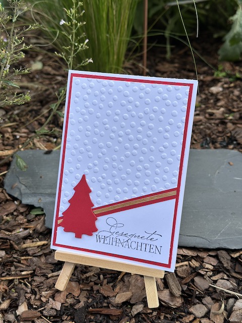 ZU sehen ist eine Weihnachtskarte ganz schlicht in weiß und grün. Der obere Teil ist mit Sternchen Muster geprägt. Auf der diagonalen Grenze zum glatten Teil ist ein Streifen gold zusehen. Als Akzent ist ein Tannenbaum angebracht. Als Spruch steht auf der Weihnachtskarte: Gesegnete Weihnachten.