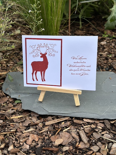 Zu sehen ist eine weiße Weihnachtskarte auf der in Glutrot ein Hirsch mit verschnörkeltem Geweih gestempelt ist. Als Spruch steht auf der Karte: VOn Herzen zauberhafte Weihnachten und alle guten Wünsche fürs neue Jahr. Gebastelt wurde die Karte mit Material von Stampin Up