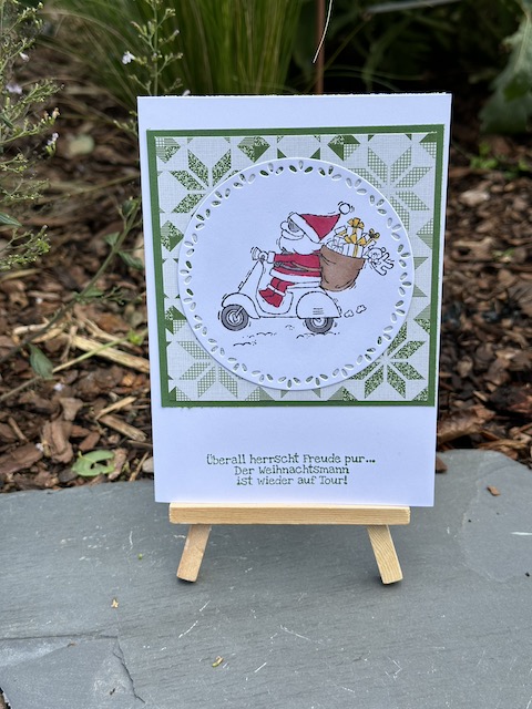 Zu sehen ist eine Weihnachtskarte. Auf dem runden Aufleger st der Weihnachtsmann auf dem Roller aus dem Stempelset von Stampin Up: "Heiter bis weihnachtlich" zu sehen. Dahinter ist befindet sich weihnachtliches Designpapier