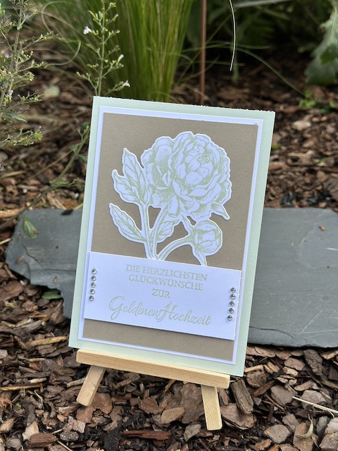 Zu sehen ist eine selbst gebastelte Karte zur goldenen Hochzeit. Eine grün gestempelte Pfingstrose ist auf einen braunen Hintergrund, der sich durch einen weißen Rand von der Lindgrünen Grundkarte abhebt. Zusätzlich ist auf der Karte noch folgender Text zu lesen: Die Herzlichsten Glückwünsche zur goldenen Hochzeit.