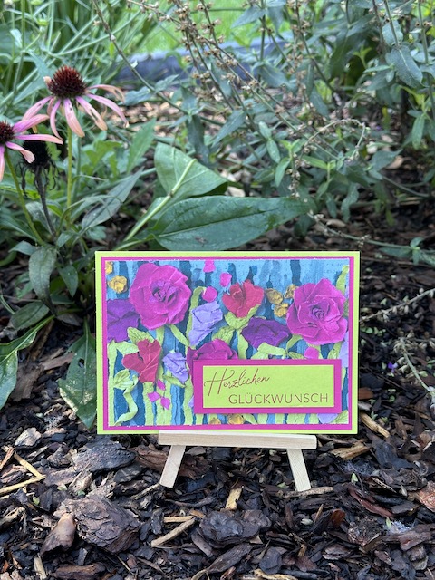 Zu sehen ist eine Glückwunschkarte zum Geburtstag. Auf einem floralen Designpapier in kräftigen Farben klebt in Limetten grün ein Etikett auf dem steht: Herzlichen Glückwunsch