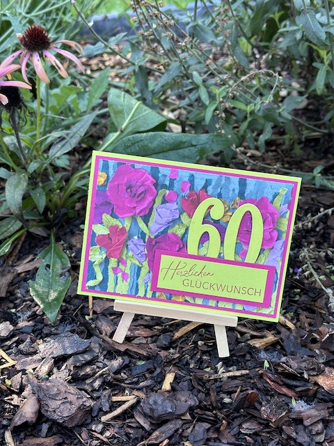 Zu sehen ist eine Glückwunschkarte zum 60. Geburtstag mit Floating Numbers. Auf einem floralen Designpapier in kräftigen Farben kleben in Limetten grün die Ziffern 6 und 0 als Floating Numbers auf der Karte. Die Karte wird ergänzt durch ein Etikett auf dem steht: Herzlichen Glückwunsch