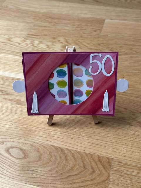 Zu sehen ist eine Ziehkulissen Karte zum 40. bzw. 50. Geburtstag. Die Geburtstagskarte zeichnet sich dadurch aus, dass man an beiden Seiten ziehen kann und man dann durch den freien Kreis auf ein Bild dahinter Blicken kann. Ist die Karte auseinandergezogen, kann sie von alleine stehen. Farblich sind es gelb und rot Töne aus Material von Stampin Up gefertigt