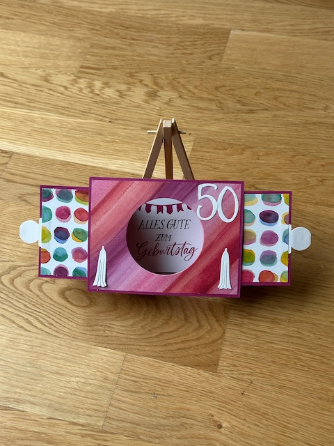 Zu sehen ist eine Ziehkulissen Karte zum 40. bzw. 50. Geburtstag. Die Geburtstagskarte zeichnet sich dadurch aus, dass man an beiden Seiten ziehen kann und man dann durch den freien Kreis auf ein Bild dahinter Blicken kann. Ist die Karte auseinandergezogen, kann sie von alleine stehen. Farblich sind es gelb und rot Töne aus Material von Stampin Up gefertigt