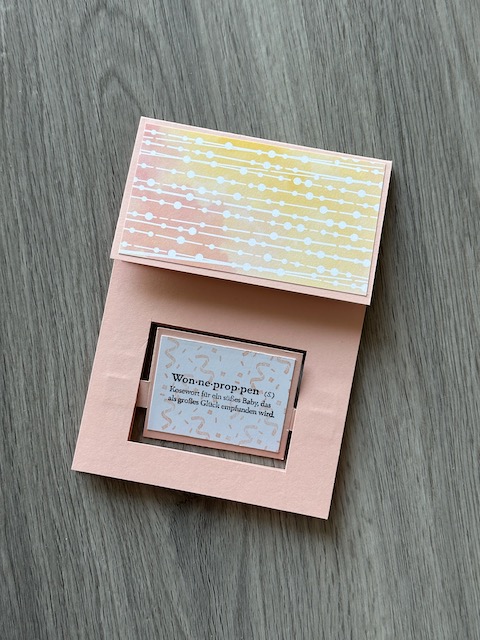 Zu sehen ist eine selbst gebastelte Babykarte mit Effekt. Unten dreht sich beim Öffnen der Karte ein Bild. Auf dem ersten Blick sieht man die Definition von Wonneproppen und nach der Drehung stehen da Glückwünsche an die stolzen Eltern. Auf der Rückseite befindet sich noch einen kleine Klappkarte, die die ganze Familie zeigt. 