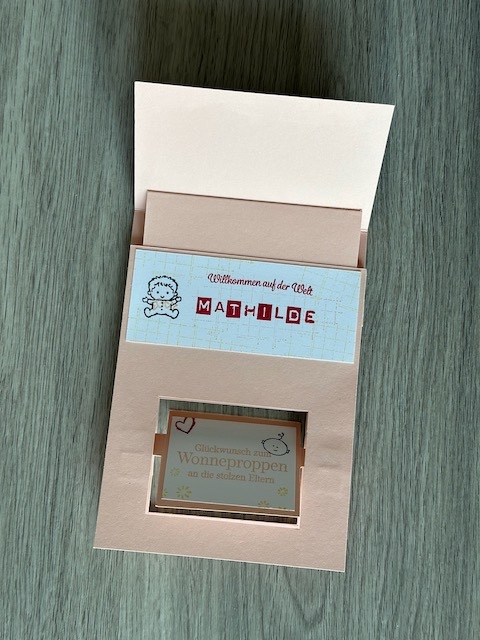Zu sehen ist eine selbst gebastelte Babykarte mit Effekt. Unten dreht sich beim Öffnen der Karte ein Bild. Auf dem ersten Blick sieht man die Definition von Wonneproppen und nach der Drehung stehen da Glückwünsche an die stolzen Eltern. Auf der Rückseite befindet sich noch einen kleine Klappkarte, die die ganze Familie zeigt.