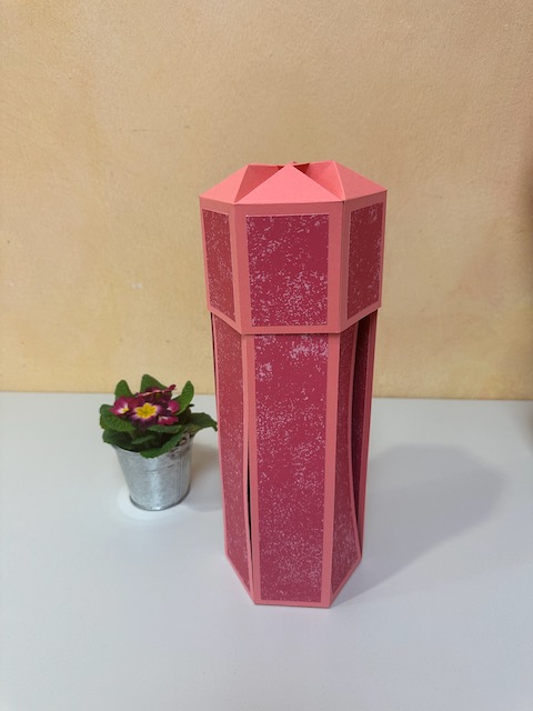 Zu sehen ist eine selbst gebastelte Verpackung für eine Weinflasche. Die Verpackung hat einen Deckel und drei Seitenteile klappen herunter, sobald man den Deckel öffnet. Es ist eine explosionsbox für eine Flasche. 