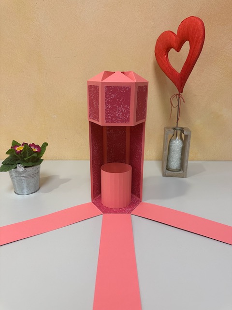 Zu sehen ist eine selbst gebastelte Verpackung für eine Weinflasche. Die Verpackung hat einen Deckel und drei Seitenteile klappen herunter, sobald man den Deckel öffnet. Es ist eine explosionsbox für eine Flasche. 