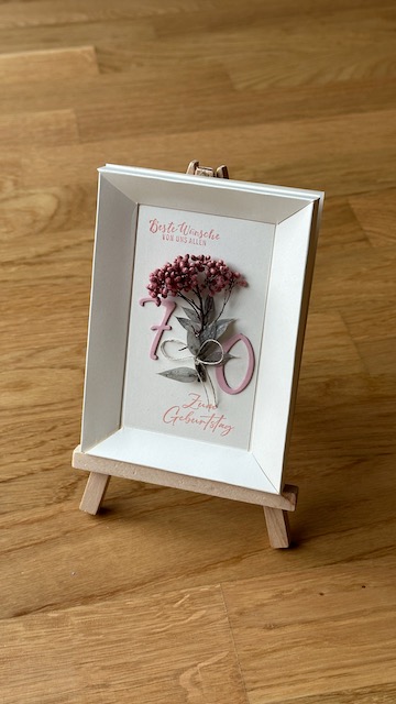 Zu sehen ist ein selbstgebastelter Shadow Rahmen in dem eine getrocknete Blume zu sehen ist kombiniert mit dem Spruch: Beste Wünsche von uns allen zum 70. Geburtstag