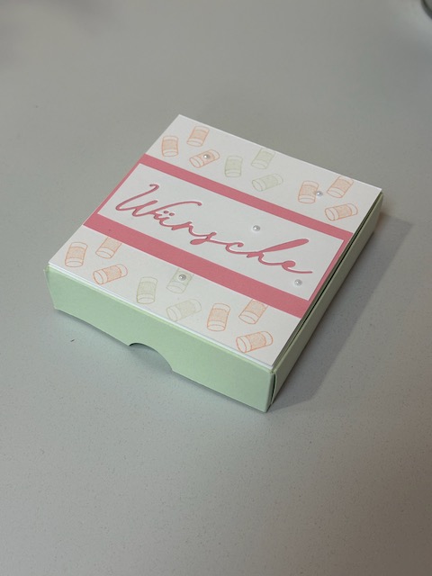 Zu sehen ist eine kleine Schachtel in grün. Oben auf ist eine Karte mit dem Wort "Wünsche" drauf zu sehen. Diese kann man wie eine Easelcard aufstellen. Klappt mann die Box auf. Erscheint die Rückansicht von einem Auto mit grüßen zur Hochzeit.