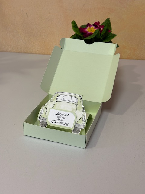 Zu sehen ist eine kleine Schachtel in grün. Oben auf ist eine Karte mit dem Wort "Wünsche" drauf zu sehen. Diese kann man wie eine Easelcard aufstellen. Klappt mann die Box auf. Erscheint die Rückansicht von einem Auto mit grüßen zur Hochzeit.