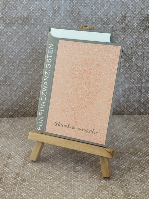 Zu sehen ist eine Geburtstagskarte, die in Buch Optik gestaltet ist. Auf dem angedeuteten Buchrücken ist das Wort Fünfundzwanzig embosst.