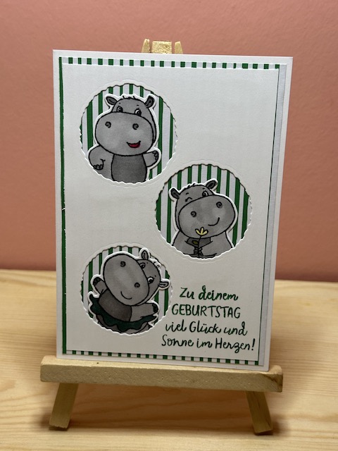 Zu sehen ist eine handmade Geburtstagskarte von Kerstins Kartenwerkstatt. Die Karte hat im weißen Layer drei Kreise ausgestanzt, aus denen jeweils ein Nilpferd mit einem lustigen Gesicht herausschaut. Hinter dem Nilpferd kann man gestreiftes Designpapier in weiß rot bzw. weiß grün sehen. Auf der Karte steht unten in der Ecke der Spruch: Zu deinem Geburtstag viel Glück und Sonne im Herzen
