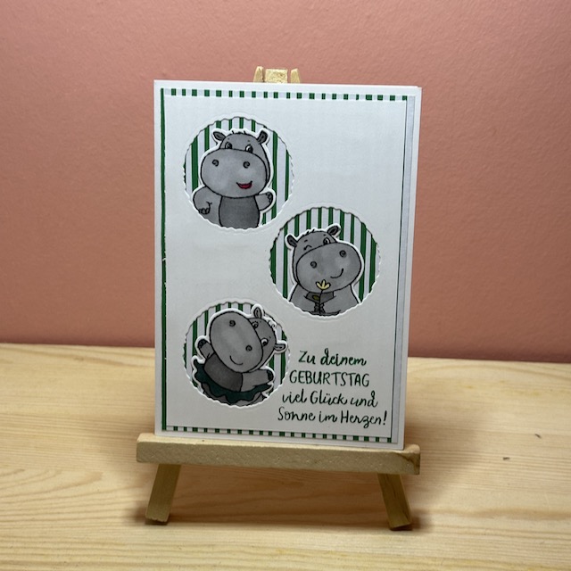 Zu sehen ist eine handmade Geburtstagskarte von Kerstins Kartenwerkstatt. Die Karte hat im weißen Layer drei Kreise ausgestanzt, aus denen jeweils ein Nilpferd mit einem lustigen Gesicht herausschaut. Hinter dem Nilpferd kann man gestreiftes Designpapier in weiß rot bzw. weiß grün sehen. Auf der Karte steht unten in der Ecke der Spruch: Zu deinem Geburtstag viel Glück und Sonne im Herzen