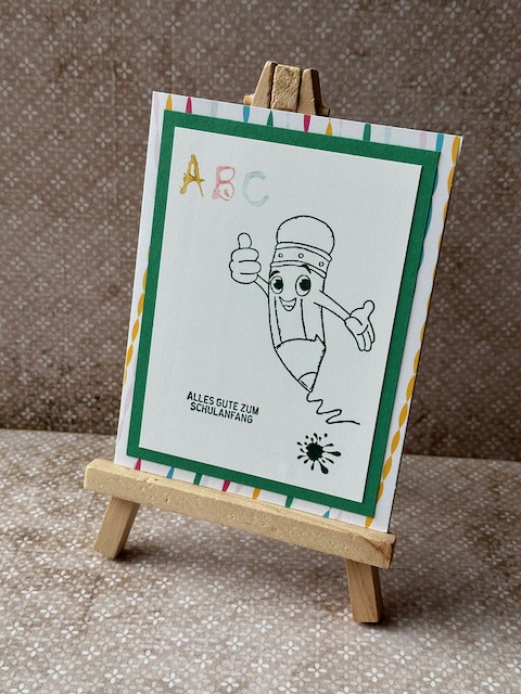 Zu sehen ist eine selbstgebastelte Karte zur Einschulung. Es ist ein Comic Stift gestempelt, der freudig einen Daumen nach oben streckt. Dazu steht auf der Karte Alles gute zum Schulanfang
