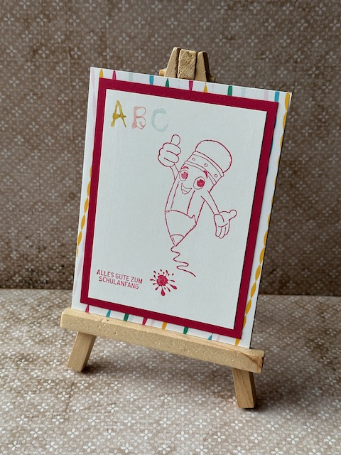 Zu sehen ist eine selbstgebastelte Karte zur Einschulung. Es ist ein Comic Stift gestempelt, der freudig einen Daumen nach oben streckt. Dazu steht auf der Karte Alles gute zum Schulanfang
