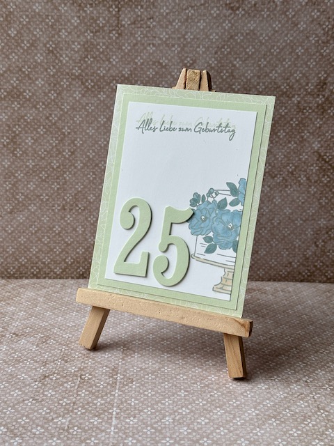 Zu sehen ist eine selbst gebastelte Geburtstagskarte in Lindgrün. Darauf ist auf einem weißen Cardstock eine zweistöckige Torte gestempelt. Die blütenverzierung auf der Torte ist in blau ausgemalt.